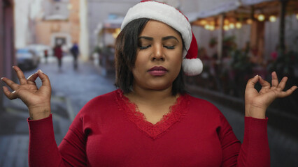 Woman meditating with closed eyes in red sweater and santa hat on urban city terrace with soft...