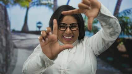 Woman smiling in an outdoor city setting, using her hands to frame a picture, expressing positivity...