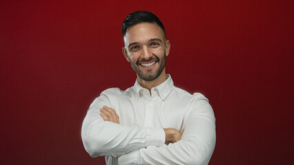 Hispanic man smiling confidently in a white shirt with arms crossed against a vibrant red...