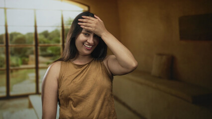 Obraz premium Young hispanic woman wearing brown tank top with eyes closed and hand on forehead in studio; mild embarrassment.