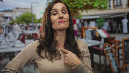 Woman with confident expression pointing at herself in a lively outdoor restaurant setting on a...