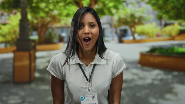 Woman smiling in a sunny park showcasing an id badge, surrounded by lush trees, creating a cheerful and professional atmosphere outdoors. - Powered by Adobe