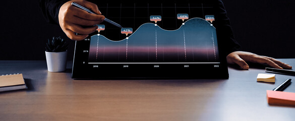 A businessperson uses a touchscreen to analyze a colorful graph in a dark office setting. The display features clear metrics and trends for effective decision-making.Noogenesis