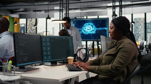 System administrator in office using AI LLM chatbot to get help optimizing performance. African american woman at work uses generative AI LLM assistant for faster software development, camera A