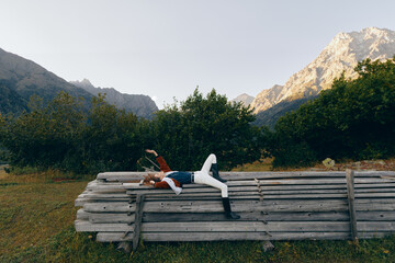 Fototapeta premium Person woman lying on logs in meadow, mountains and forest background, nature relaxation and outdoors resting pose during travel or escape, peaceful countryside scene with greenery
