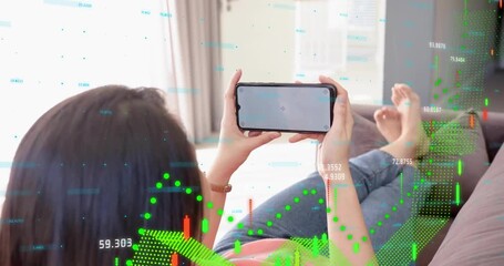 Woman reclining on sofa holding phone, tapping and raising, revealing finance candlestick overlays - Powered by Adobe