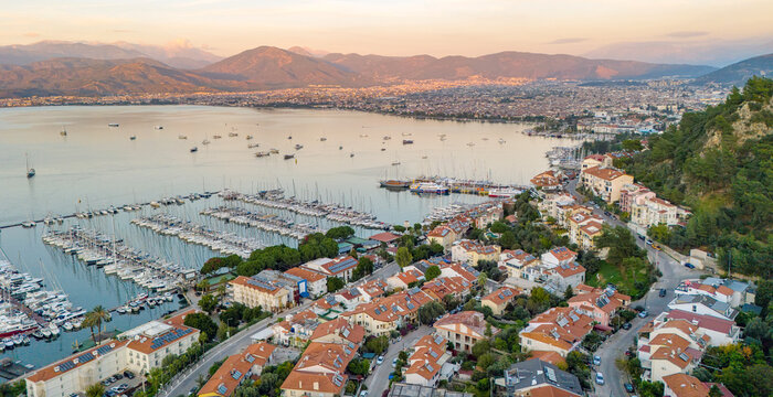 Panoramic aerial view of Fethiye city center and marina in Turkey featuring the harbor full of boats and the surrounding mountains during a beautiful golden sunset evening