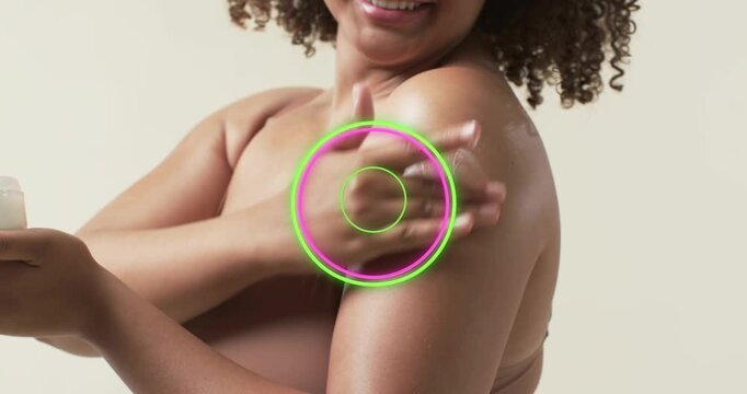 Woman scooping cream from jar, smoothing shoulder while rings pulsing over area for skincare