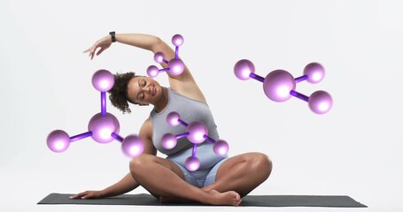 Woman opening eyes, looking right, moving into yoga stretch on black mat, molecules floating around