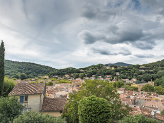 Elevated view over Collobrieres, a provencal village in Var, Provence, tiled rooftops nestled among the Maures hills under dramatic clouds. Houses spread illustrate a typical Provence settlement.