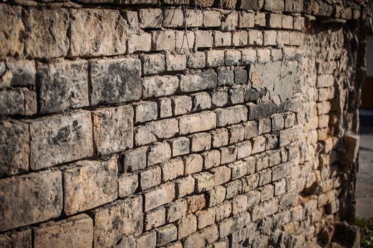 Close view of a crumbling brick wall shows weathered masonry with cracks, missing mortar, and textured stone, capturing decay and age in an urban setting, emphasizing surface detail and deterioration. - Powered by Adobe