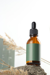 Amber bottle with green label and dropper on a stone surface with dried plant decoration