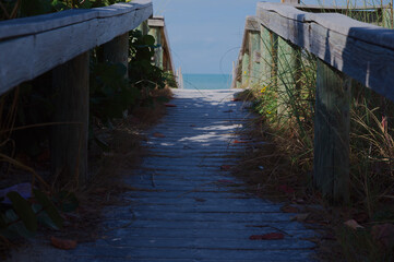 Sunny Beach Path With Weathered Wooden Railings Leading To Quiet Sea View at St. Pete Beach, FL. Sandy path opening to a calm blue sea. Ideal for travel, coastal lifestyle, relaxation, and nature them