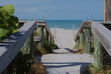 Sunny Beach Path With Weathered Wooden Railings Leading To Quiet Sea View at St. Pete Beach, FL. Sandy path opening to a calm blue sea. Ideal for travel, coastal lifestyle, relaxation, and nature them
