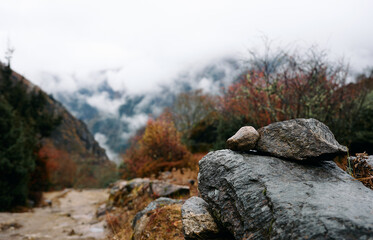 Gray rocks rest on the path in a mountainous area with clouds covering peaks in the distance during a foggy day