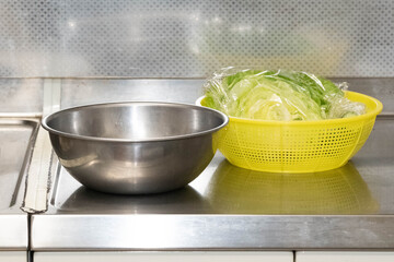 ラップに包まれた野菜の入ったザルとボウル