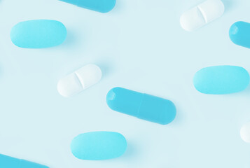Scattered blue and white pills on a light blue surface creating a clean and minimalist composition