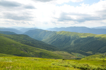 Fototapeta premium Breathtaking mountain landscape with rolling green hills and a deep valley under a cloudy sky. Perfect for nature, travel, and outdoor lifestyle scenes conveying calm, vastness, and natural beauty