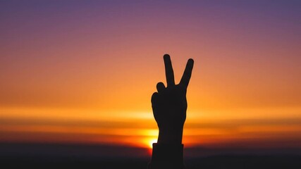 Silhouette hand gesture showing peace sign against sunset sky background
