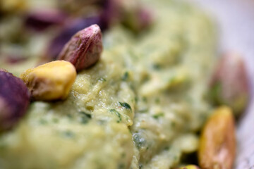 Soft focus macro shot of a pistachio paste dessert or dip emphasizing the chunks of nuts and the creamy green base of the sweet treat