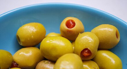 Close up of a blue bowl filled with green olives stuffed with red pimento peppers serving as a classic mediterranean appetizer or snack