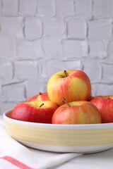 Ripe red apples in bowl on white table near grey textured wall, closeup. Space for text
