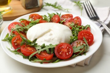 Delicious burrata cheese with arugula and tomatoes on light table, closeup