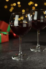 Glasses of red wine and Christmas decor on grey table against background with blurred lights