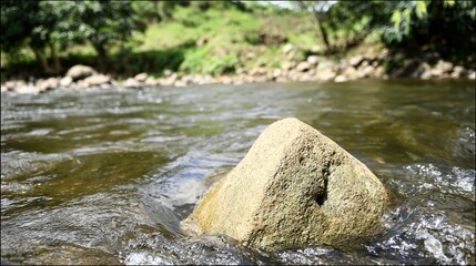 pebble. Large river stone lodged in a fast-flowing stream with water parting around it. travel magazines, destination branding, designed for outdoor magazines and nature guides.