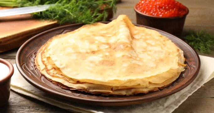 Adding red caviar to tasty crepes at wooden table, closeup