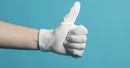 Woman in cloth glove showing thumbs up on light blue background, closeup