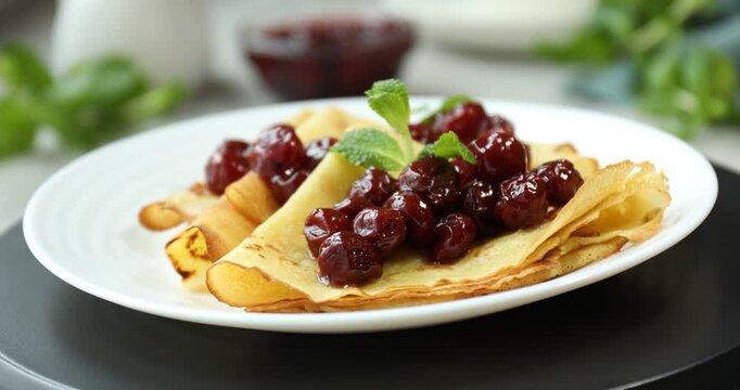 Tasty crepes with cherries and mint on table, spinning. Closeup view