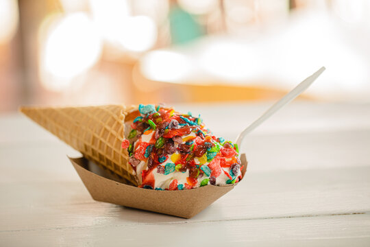 A vanilla ice cream cone topped with colorful fruity pebbles cereal