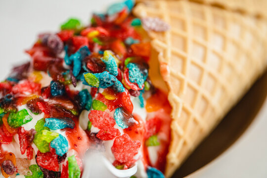 A vanilla ice cream cone topped with colorful fruity pebbles cereal
