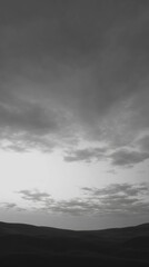Obraz premium A serene black-and-white landscape featuring rolling hills and a cloudy sky, evoking a sense of calm and introspection.