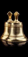 Two golden bells sit closely together on a reflective black surface Metallic