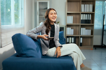 Obraz premium Asian businesswoman relaxing on couch using smartphone