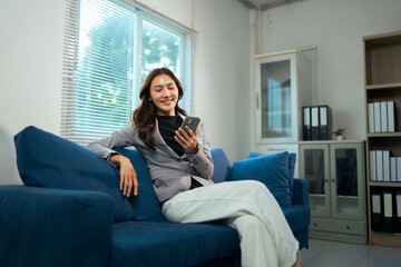 Obraz premium Asian businesswoman relaxing on sofa using smartphone