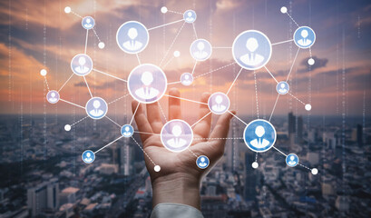 A human hand reaches out towards a digital network of connected people icons, symbolizing communication, technology, and social connections in an urban landscape. Tessel