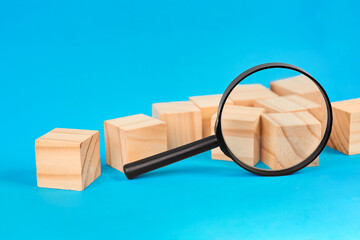 A magnifying glass focusing on scattered cubes to represent detailed inspection analysis discovery and careful evaluation.
