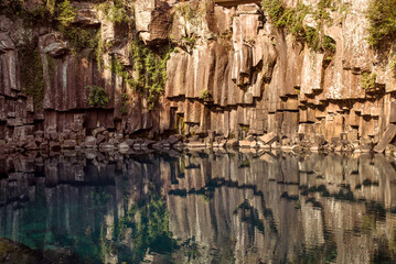 Cheonjeyeon Waterfall, Stunning basalt columns reflect in tranquil waters, showcasing the natural beauty of Jeju Island, South Korea