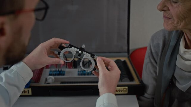 Close up shot of white haired senior woman talking to ophthalmologist during exe exam in clinic and looking at trial frames asking questions