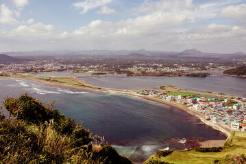 Seongsan Ilchulbong, Jeju Islands, South Korea, 10.10.2015: A captivating view of Jeju Islands coastline, featuring vibrant homes nestled against the backdrop of rolling hills and the ocean