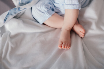 Close-up view of a baby sitting on a soft blanket with legs crossed. The clean, bright background and pastel clothing create a peaceful and minimalistic scene, suitable for concepts of infancy