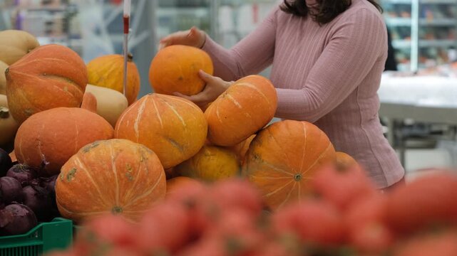 Woman choosing pumpkins in supermarket produce section, comparing color and size, shopping and healthy food lifestyle concept