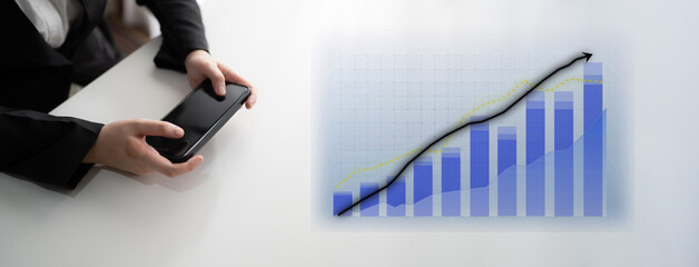 A business person holds a smartphone while reviewing a financial growth chart. This modern office setting emphasizes the importance of data analysis in achieving success. Impute