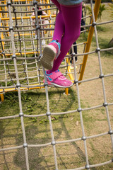 A child climbing a rope net structure with pink tights and sneakers, highlighting active outdoor play.
