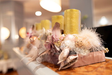 Elegant pastel Christmas décor featuring gold candles, feathers, ornaments, and soft bokeh lights. A warm, luxurious holiday arrangement perfect for festive designs.