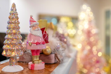 Fototapeta premium A pastel Christmas decoration scene featuring a pink Santa figurine and a glittery tree, captured with soft golden bokeh lights. Warm, festive, and perfect for holiday-themed designs.