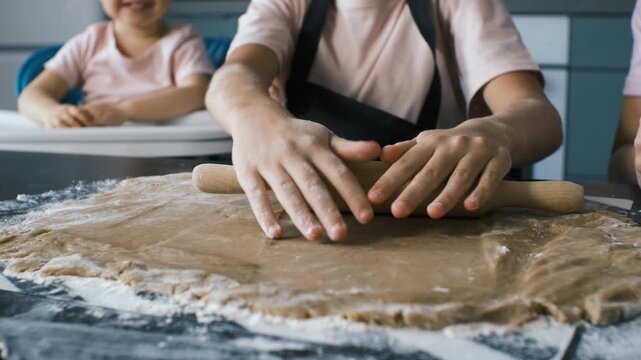 Hands press a rolling pin over ginger cookie dough on a floured kitchen surface, highlighting the tactile steps of homemade baking as a mother and daughters enjoy warm family cooking time concept - Powered by Adobe